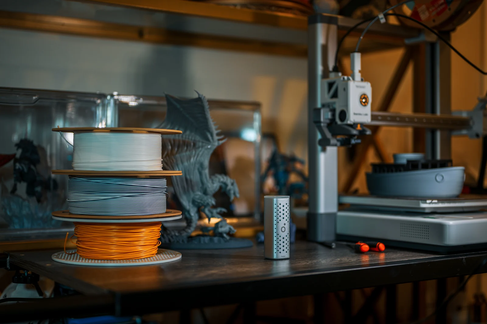 An Airo TVOC Pod on a workbench beside a 3D printer, filament spools and printed models.